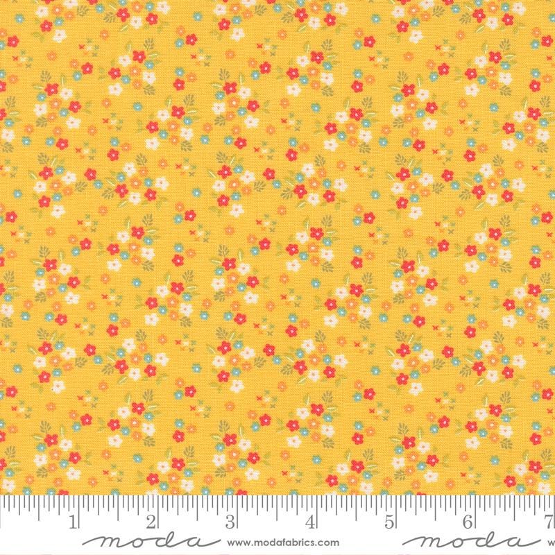 The image is a fabric with a yellow background and a pattern of small flowers in various colors, including red, white, and green.