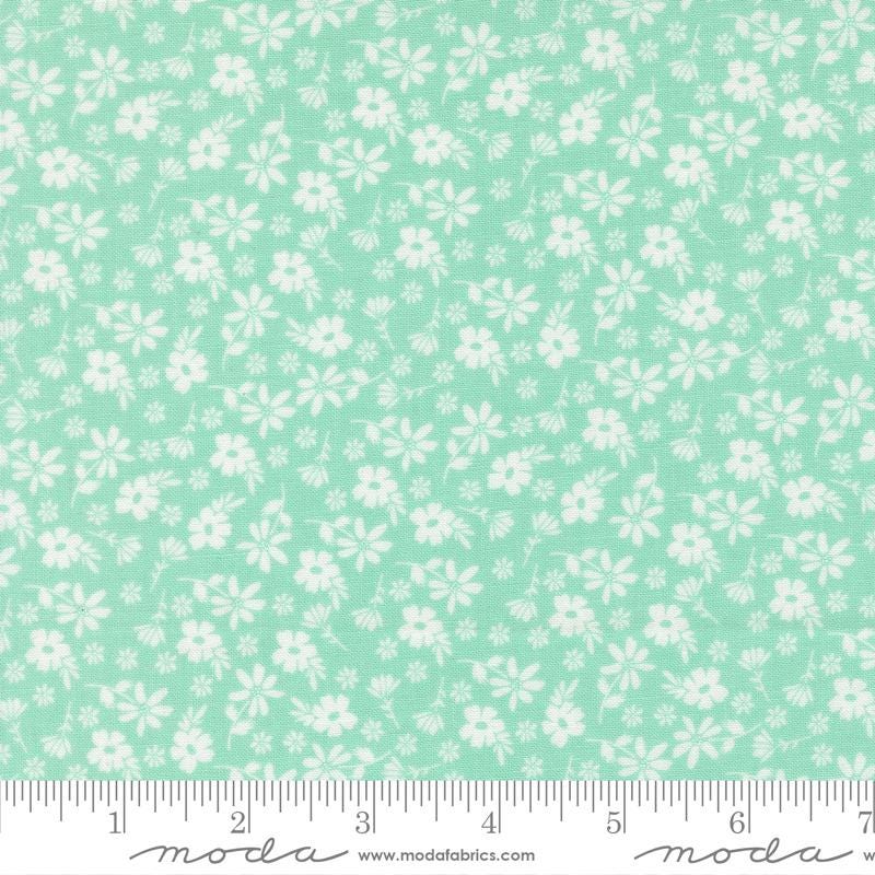 a fabric with a light green floral pattern, consisting of white flowers scattered across the fabric. The fabric is laid out on a ruler for size comparison.