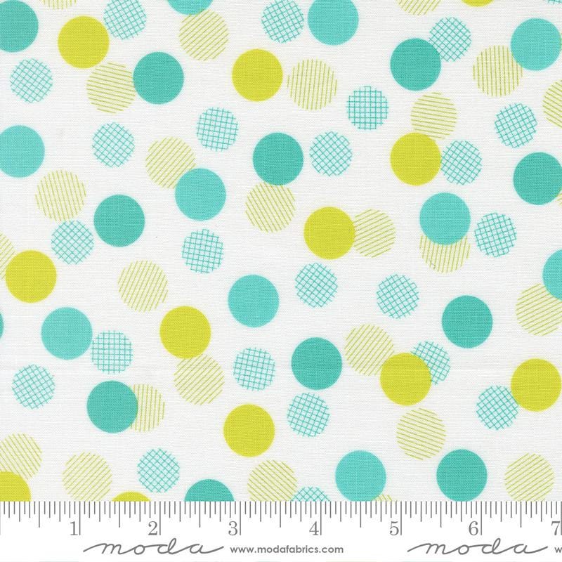 a white fabric with a pattern of multicolored polka dots in various shades of green, yellow, and blue. The fabric appears to be a textile or material with a playful and vibrant design.