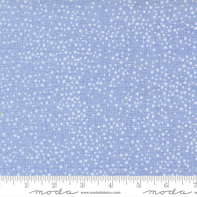 The image is a close-up of a fabric with a light blue background and white dots, resembling a speckled or speckled pattern.