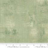 The image is a close-up of a textured green fabric with a ruler for scale.