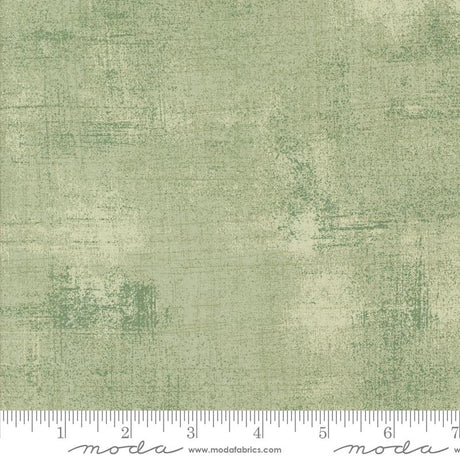 The image is a close-up of a textured green fabric with a ruler for scale.