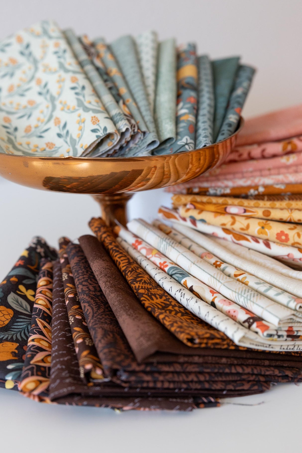 A collection of colorful fabric swatches arranged in a bowl, with a copper-colored bowl holding the swatches.