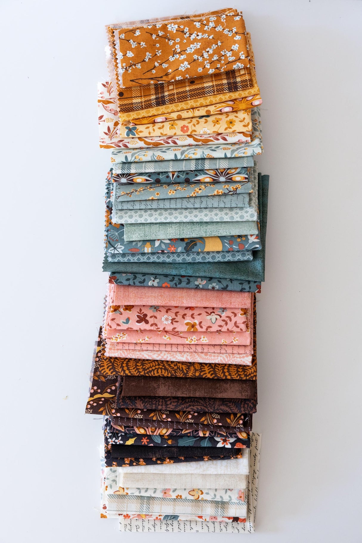 A stack of various fabric swatches in different patterns and colors, arranged neatly on a white surface.