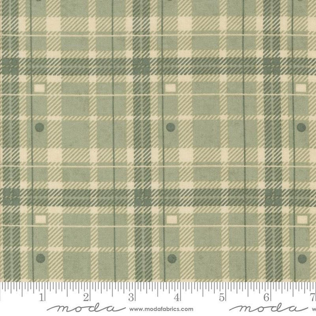 a fabric with a green and beige plaid pattern, featuring a repeating diagonal grid-like design. The fabric appears to be a textile or material with a plaid pattern, which is a type of textile design characterized by diagonal or crisscrossing lines. The fabric is displayed on a ruler for scale, indicating its size or dimensions.
