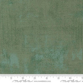 The image is a close-up of a textured green fabric with a ruler for scale.
