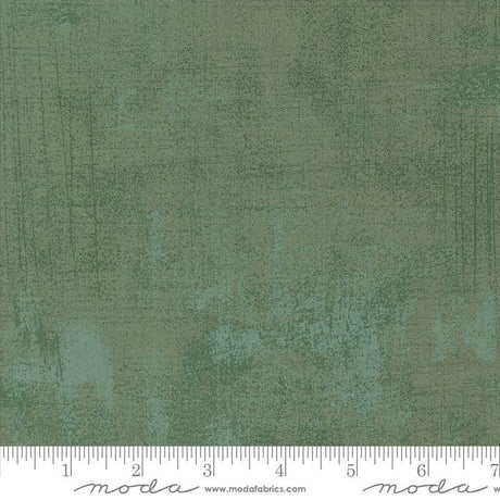 The image is a close-up of a textured green fabric with a ruler for scale.