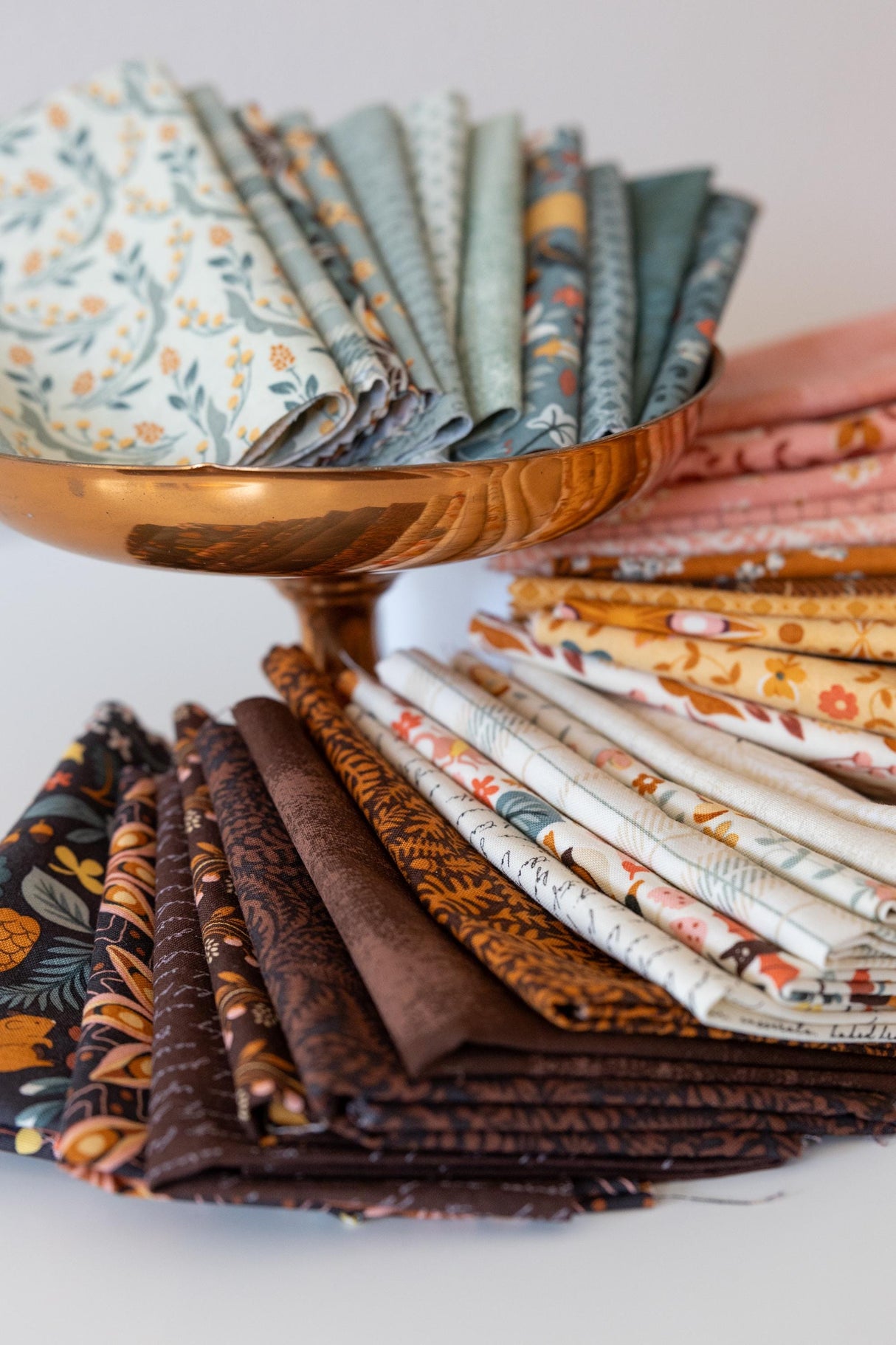 A collection of colorful fabric swatches arranged in a bowl, with a copper-colored bowl holding the swatches.