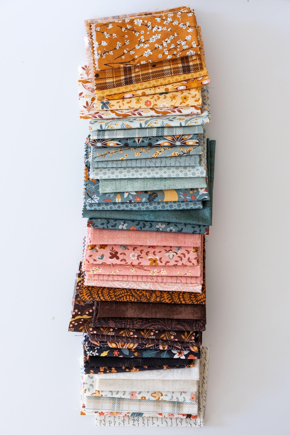 A stack of various fabric swatches in different patterns and colors, arranged neatly on a white surface.