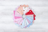 A circular arrangement of various fabric swatches in different colors and patterns, including pink, white, blue, and red, on a white wooden surface.