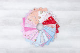 A circular arrangement of various fabric swatches in different colors and patterns, including pink, white, blue, and red, on a white wooden surface.