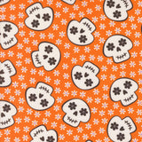 a repeating pattern of stylized skull faces on an orange background with white flowers.