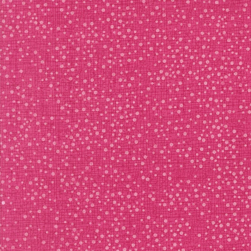 The image is a close-up of a pink fabric with small white dots or specks scattered across it, creating a textured and speckled appearance.