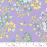 The image is a fabric with a purple background and a repeating pattern of green and yellow leaves and flowers.