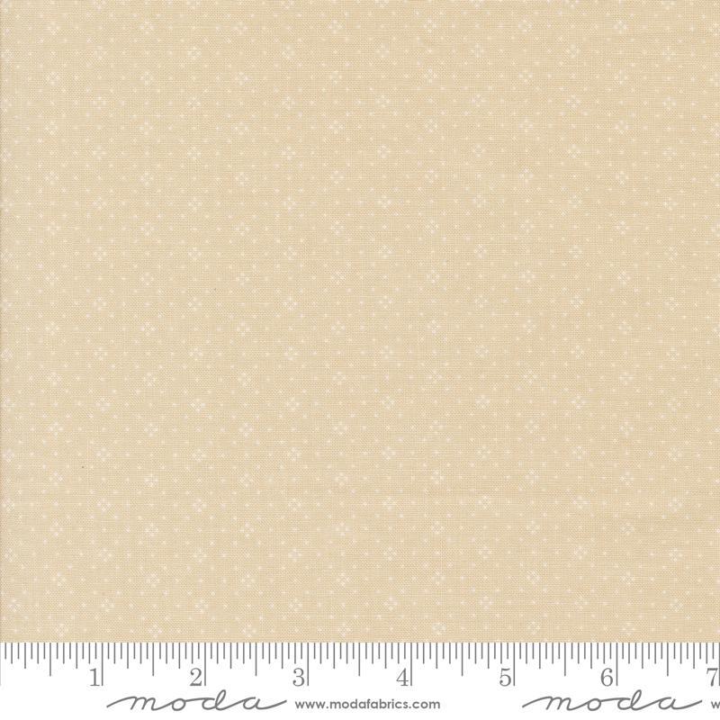 The image is a fabric sample with a light beige pattern, featuring small white dots or stars. The fabric is displayed on a ruler for scale, indicating its size.