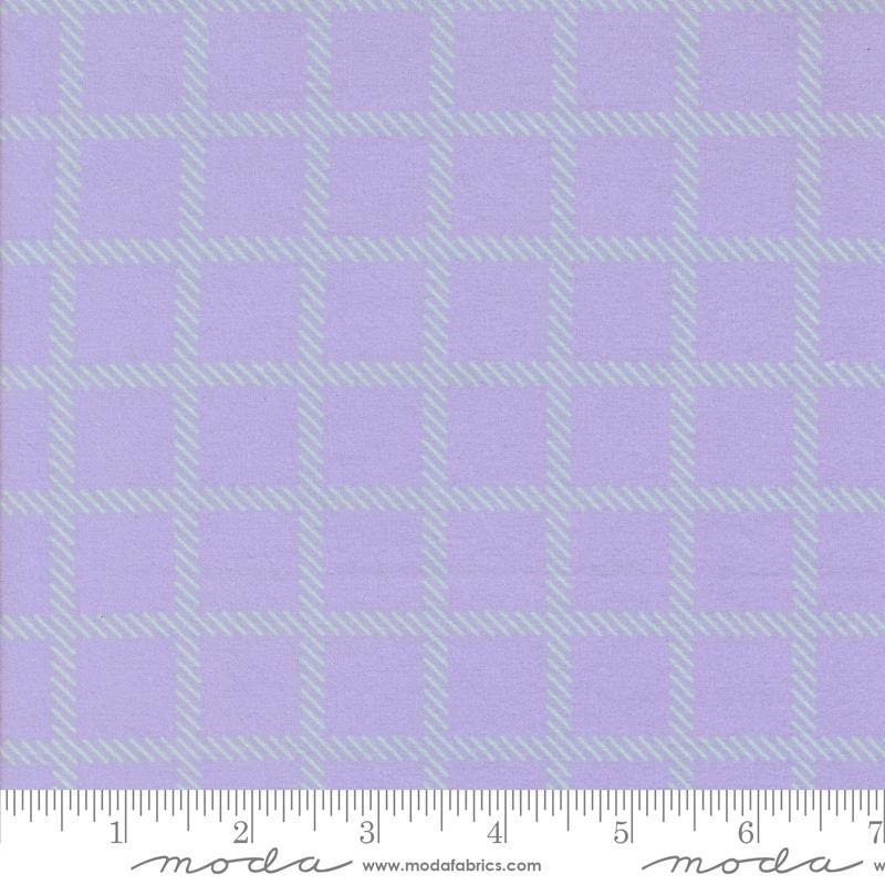 a fabric with a purple and green checkered pattern. The fabric appears to be a fabric with a grid-like design, with squares and rectangles in shades of purple and green. The fabric is displayed on a ruler for scale, indicating its size.
