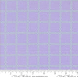 a fabric with a purple and green checkered pattern. The fabric appears to be a fabric with a grid-like design, with squares and rectangles in shades of purple and green. The fabric is displayed on a ruler for scale, indicating its size.
