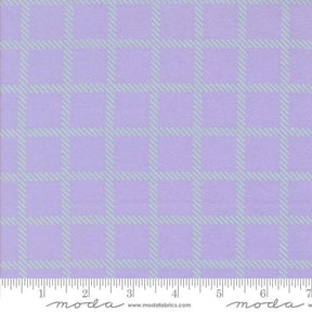 a fabric with a purple and green checkered pattern. The fabric appears to be a fabric with a grid-like design, with squares and rectangles in shades of purple and green. The fabric is displayed on a ruler for scale, indicating its size.