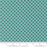 The image is a fabric with a repeating pattern of small blue flowers and white x's. The pattern is arranged in a diagonal direction, creating a sense of movement across the fabric. The fabric appears to be made of a material with a light blue-green hue, and there is a ruler visible at the bottom of the image, indicating the fabric's size.