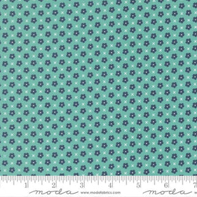 The image is a fabric with a repeating pattern of small blue flowers and white x's. The pattern is arranged in a diagonal direction, creating a sense of movement across the fabric. The fabric appears to be made of a material with a light blue-green hue, and there is a ruler visible at the bottom of the image, indicating the fabric's size.