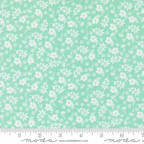 a fabric with a light green floral pattern, consisting of white flowers scattered across the fabric. The fabric is laid out on a ruler for size comparison.