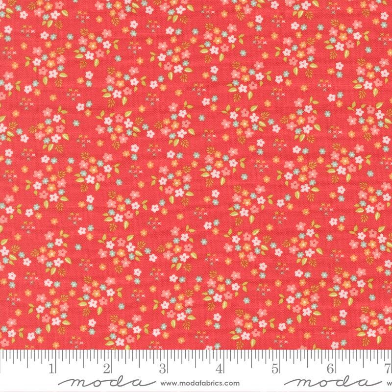 The image is a vibrant red fabric with a repeating pattern of small white and pink flowers and leaves. The fabric appears to be a fabric with a floral print, and it is displayed on a ruler for size reference.