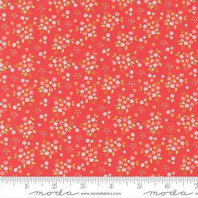 The image is a vibrant red fabric with a repeating pattern of small white and pink flowers and leaves. The fabric appears to be a fabric with a floral print, and it is displayed on a ruler for size reference.