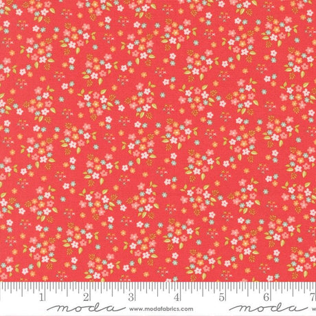 The image is a vibrant red fabric with a repeating pattern of small white and pink flowers and leaves. The fabric appears to be a fabric with a floral print, and it is displayed on a ruler for size reference.
