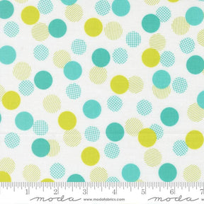 a white fabric with a pattern of multicolored polka dots in various shades of green, yellow, and blue. The fabric appears to be a textile or material with a playful and vibrant design.