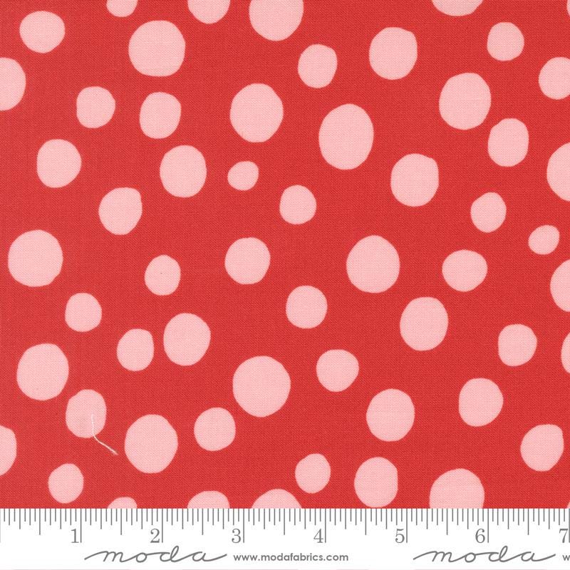 a close-up view of a red fabric with white polka dots. The fabric appears to be a part of a larger textile or garment, as indicated by the ruler for scale.