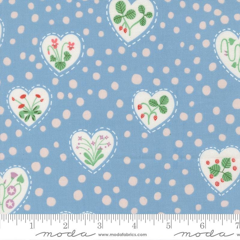 The image is a fabric with a blue background and white polka dots. It features heart-shaped designs with flowers and leaves, as well as other heart-shaped designs with flowers and leaves.
