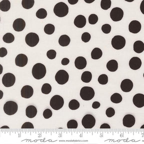 a close-up view of a fabric with a black and white polka dot pattern. The fabric is white with numerous black polka dots scattered across it. There is a ruler placed at the bottom of the image, indicating the size of the fabric.