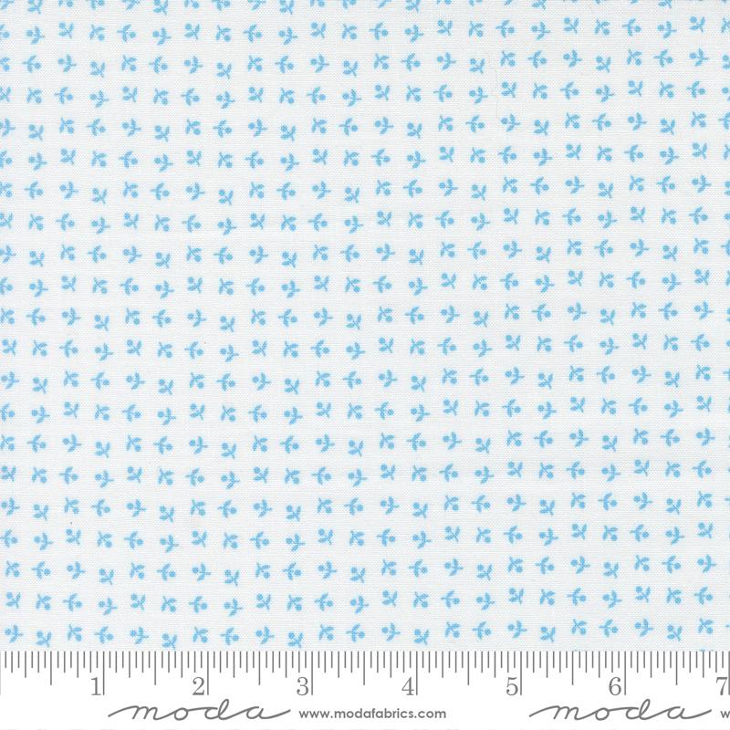 The image is a fabric with a repeating pattern of small blue flowers or leaves. The pattern is evenly spaced and covers the entire fabric. The fabric appears to be made of a light-colored material, possibly cotton or linen. The image does not contain any text or other objects, and the focus is solely on the pattern and color of the fabric.