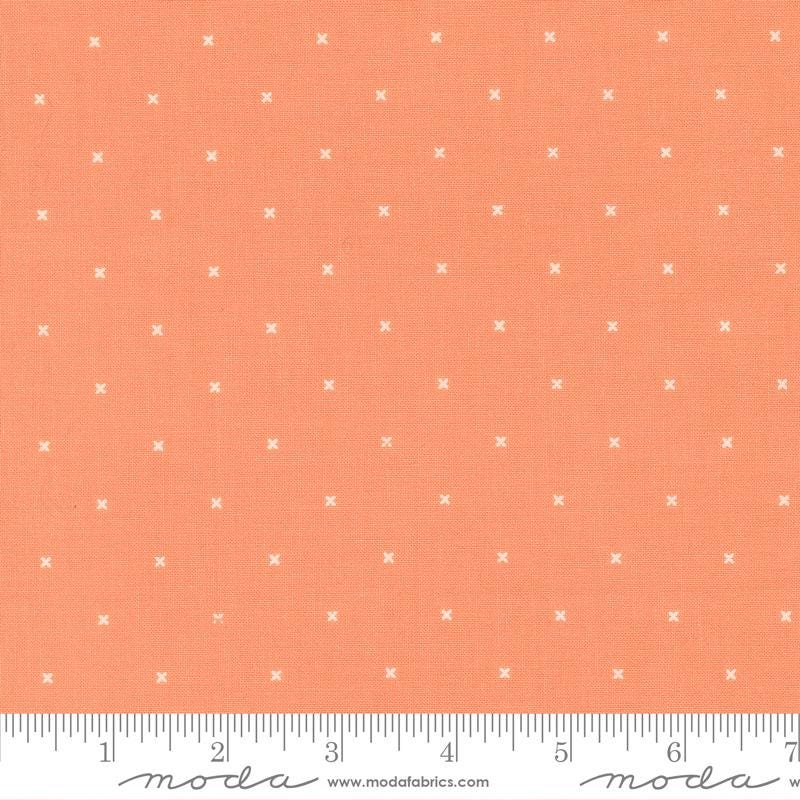 The image is a fabric with a repeating pattern of small white crosses or dots on an orange background.
