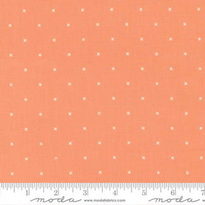 The image is a fabric with a repeating pattern of small white crosses or dots on an orange background.
