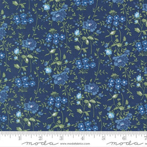 a close-up view of a fabric with a floral pattern in shades of blue and green. The pattern consists of various blue flowers and green leaves arranged in a repeating design across the fabric. The fabric appears to be a dark blue color, and the pattern is detailed and intricate.
