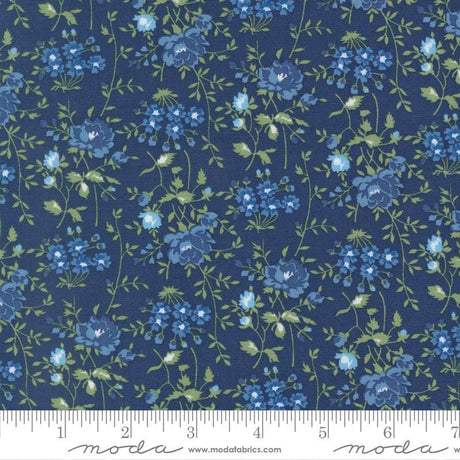 a close-up view of a fabric with a floral pattern in shades of blue and green. The pattern consists of various blue flowers and green leaves arranged in a repeating design across the fabric. The fabric appears to be a dark blue color, and the pattern is detailed and intricate.