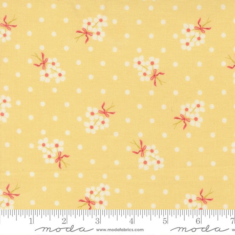 The image is a fabric with a yellow background and white polka dots, featuring small white flowers with pink bows.