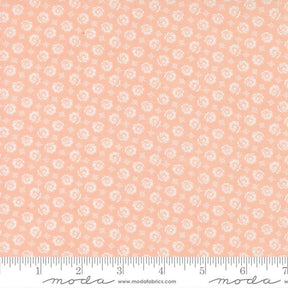 The image is a fabric with a repeating pattern of small white flowers or circles on a peach-colored background.