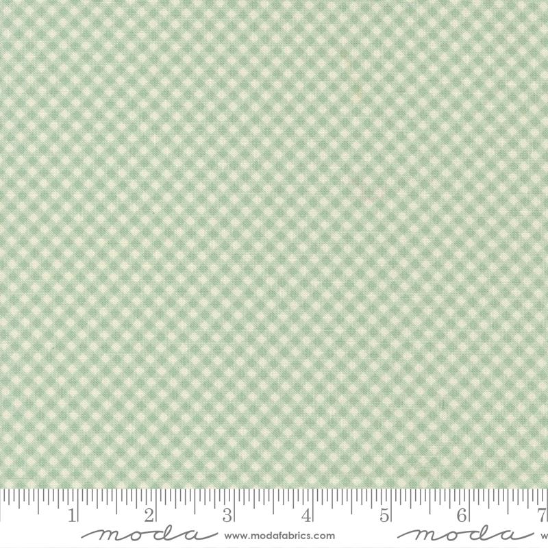 a fabric with a green and white checkered pattern. The fabric appears to be a gingham pattern, which is a type of fabric with a diagonal grid-like pattern of squares. The fabric is displayed on a ruler for scale, indicating its size.