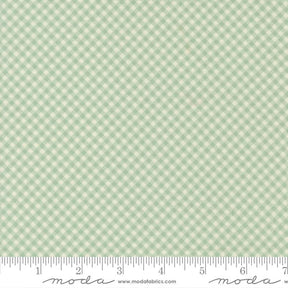 a fabric with a green and white checkered pattern. The fabric appears to be a gingham pattern, which is a type of fabric with a diagonal grid-like pattern of squares. The fabric is displayed on a ruler for scale, indicating its size.
