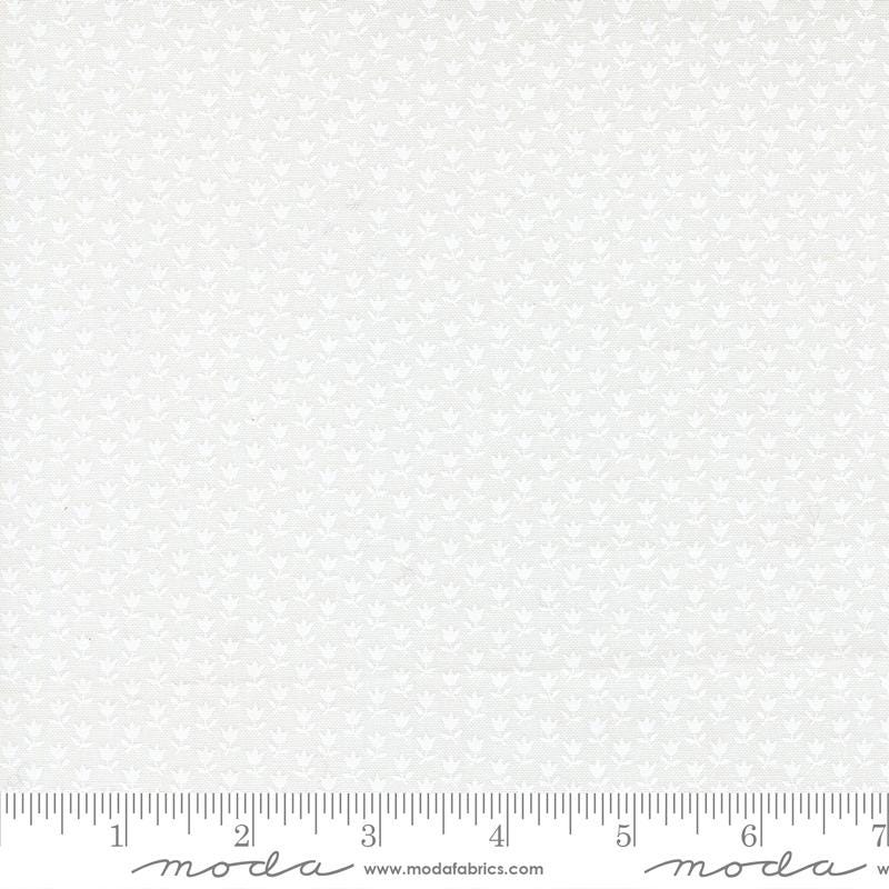 The image is a white fabric with a repeating pattern of small white flowers or leaves. The fabric appears to be a type of lace or sheer material, as it has a delicate and intricate design. The fabric is displayed on a ruler for scale, indicating its size.