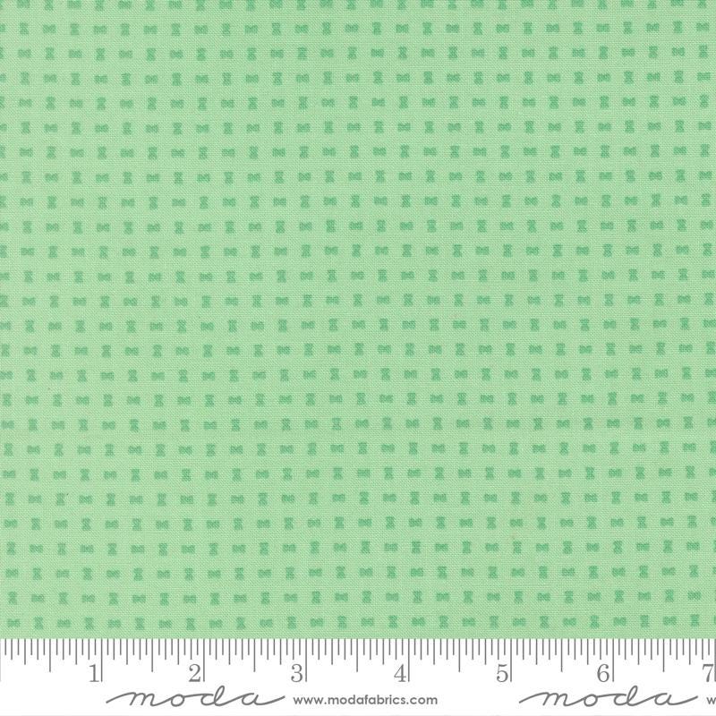The image is a fabric with a green pattern, featuring small square shapes arranged in a grid-like pattern.