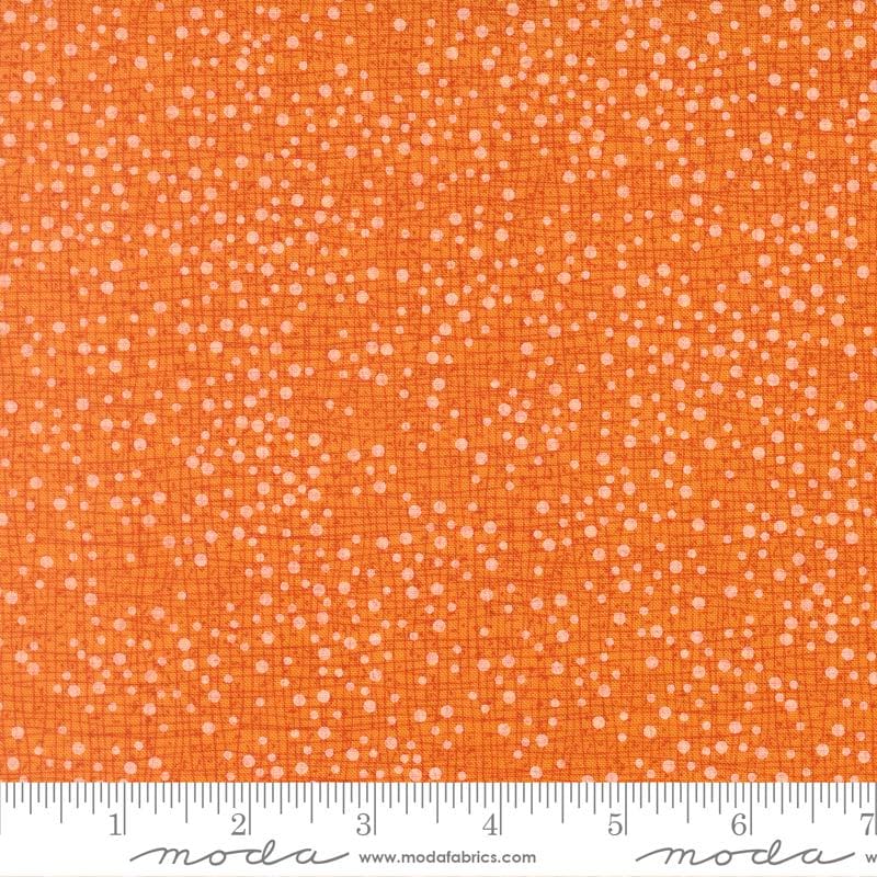 The image is a close-up of a fabric with a pattern of small white dots or specks on an orange background.