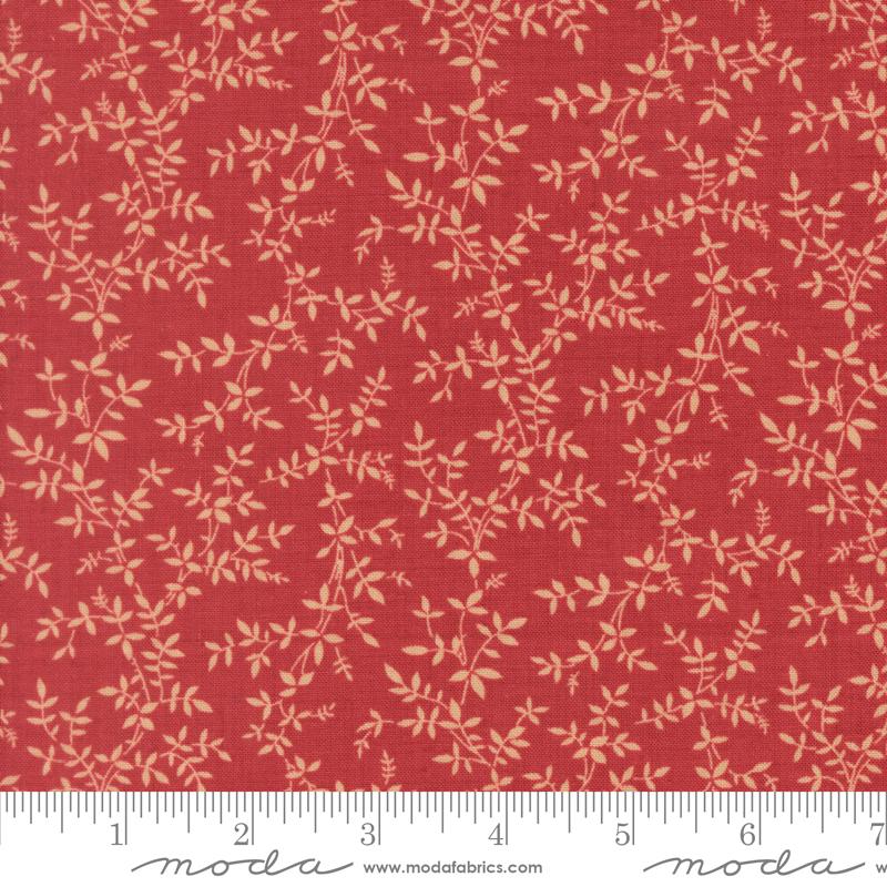 a close-up view of a fabric with a red background and a repeating pattern of small white leaves or flowers. The fabric appears to be made of a material with a floral print, and there is a ruler visible at the bottom of the image.